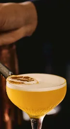 Hand garnishing a cocktail with a slice of citrus in a cosy hotel bar setting.