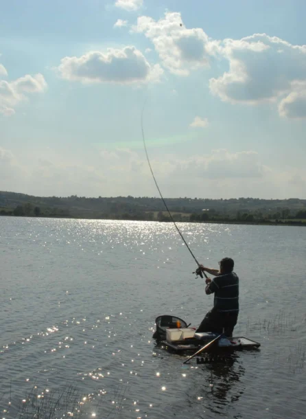 A person fishing on a serene lake under a bright, cloudy sky near Hotel Kilmore.
