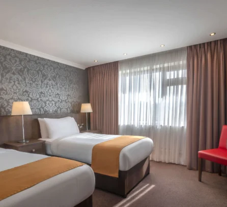 Cosy hotel room with two beds, elegant wallpaper, and soft lighting for a warm stay.