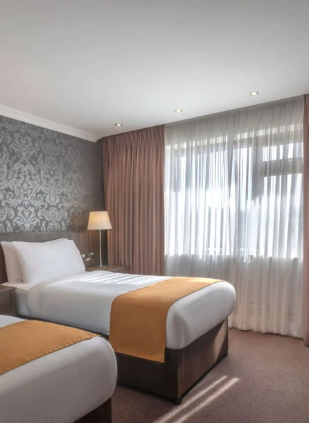 Cosy hotel room with two beds, elegant wallpaper, and soft lighting for a warm stay.