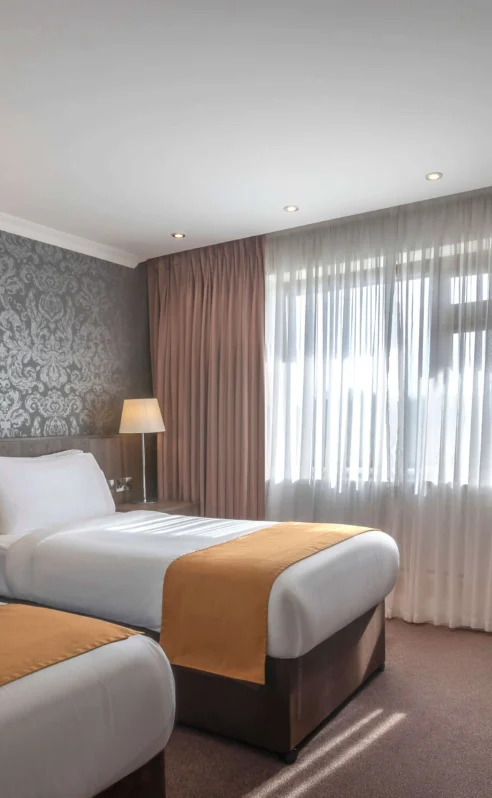 Cosy hotel room with two beds, elegant wallpaper, and soft lighting for a warm stay.