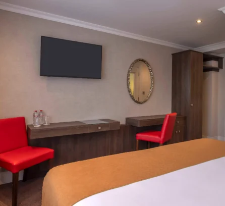 Comfortable hotel room with cosy bed, red chairs, and a mounted TV for guests to relax.