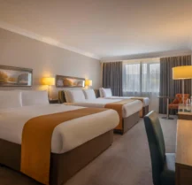 Spacious hotel room with three large beds, warm lighting, and cosy seating area.