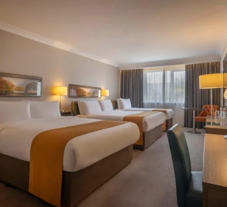 Spacious hotel room with three large beds, warm lighting, and cosy seating area.