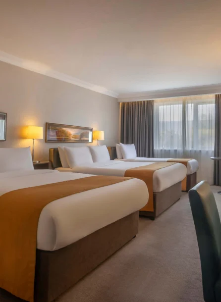 Spacious hotel room with three large beds, warm lighting, and cosy seating area.