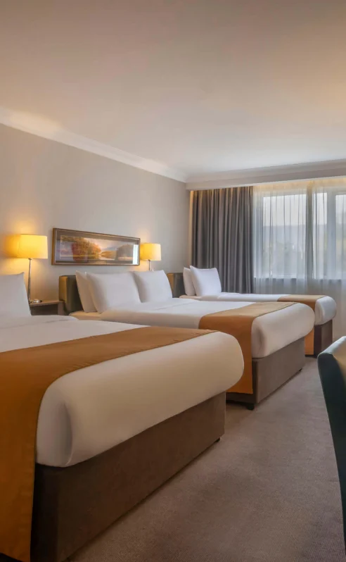 Spacious hotel room with three large beds, warm lighting, and cosy seating area.
