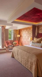 Luxurious hotel room with king bed, elegant decor, and scenic garden view through large window.