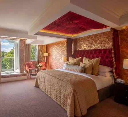 Luxurious hotel room with king bed, elegant decor, and scenic garden view through large window.