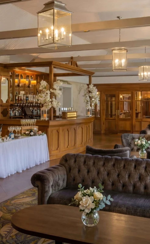 Cosy hotel lounge with a welcoming bar, floral decorations, and plush seating.
