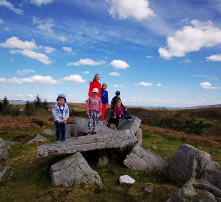Family enjoying a sunny day on a rocky hill with a panoramic countryside view.