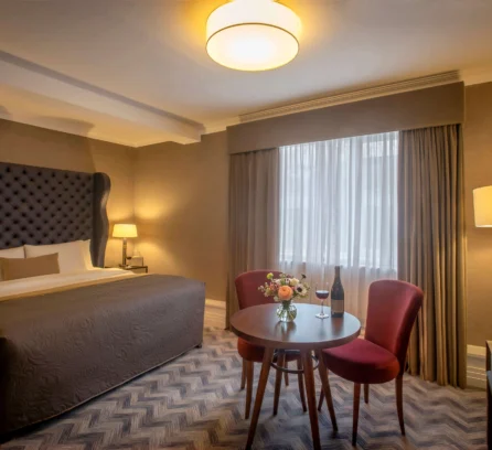 Elegant hotel room with a cosy seating area, flowers, and wine, perfect for relaxation.