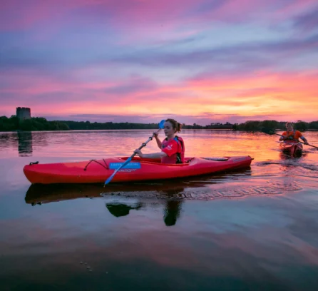 Family kayaking on calm lake at sunset near Hotel Kilmore, vibrant sky reflecting on water.