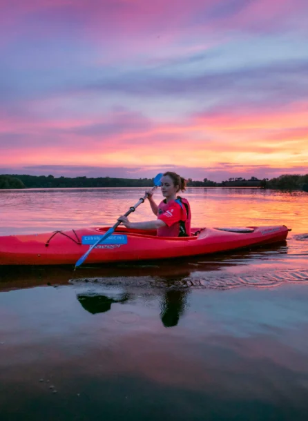 Family kayaking on calm lake at sunset near Hotel Kilmore, vibrant sky reflecting on water.