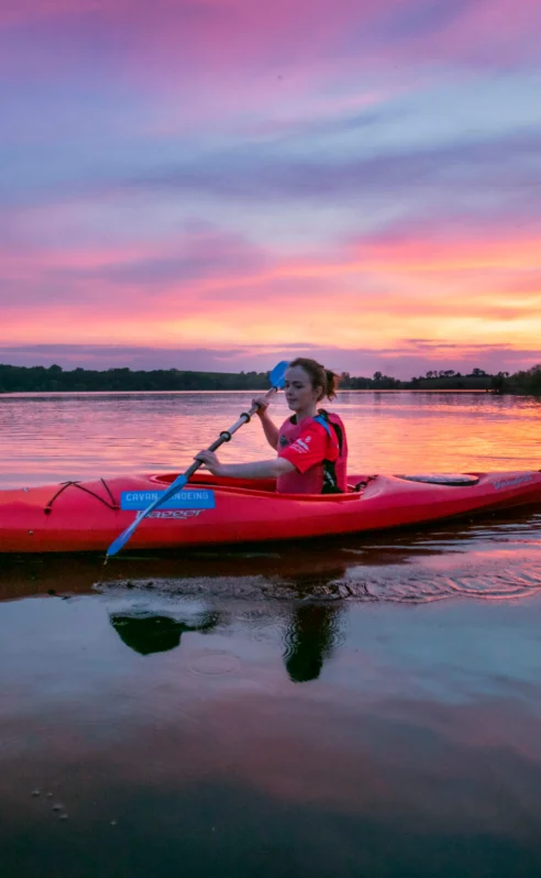 Family kayaking on calm lake at sunset near Hotel Kilmore, vibrant sky reflecting on water.
