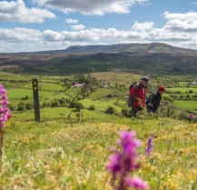 A couple hiking through lush hills near Hotel Kilmore under a bright blue sky.