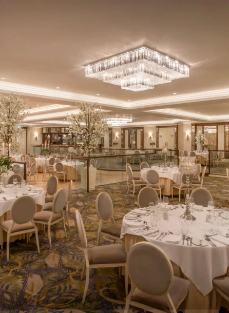 Elegant hotel dining room set for an event, tables adorned with white linens and floral centrepieces.