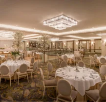 Elegant hotel ballroom with round tables set for an event, under dazzling chandeliers.