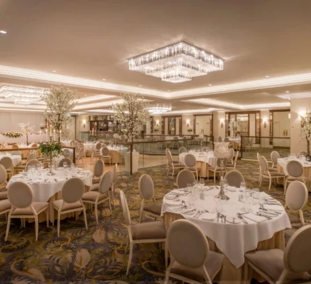 Elegant hotel ballroom with round tables set for an event, under dazzling chandeliers.