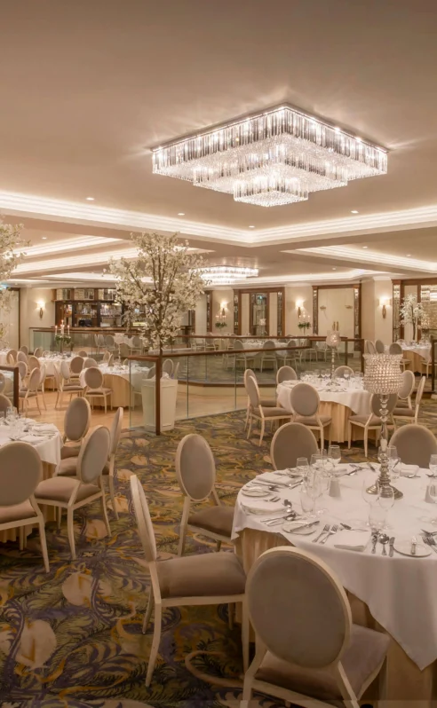 Elegant hotel ballroom with round tables set for an event, under dazzling chandeliers.