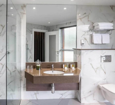 Modern hotel bathroom with marble tiles, glass shower, and neatly arranged toiletries.