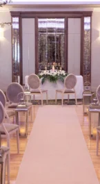 Elegant hotel event space set for a wedding ceremony with floral decorations and aisle seating.