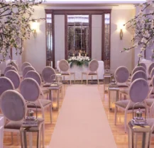 Elegant hotel event space set for a wedding ceremony with floral decorations and aisle seating.