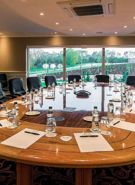 Spacious hotel conference room with a large table set for a meeting, overlooking lush greenery.
