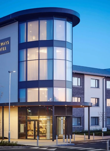 Modern hotel with a welcoming entrance, reflecting a warm evening glow. Families and couples arriving.